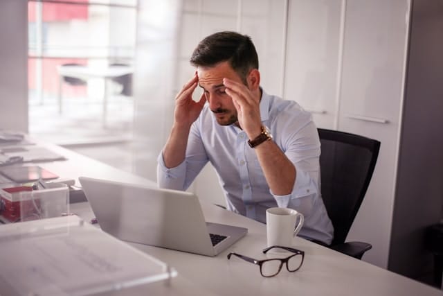 Business professional stressed while reviewing finances at his desk, representing the tax planning challenges of a high-income year