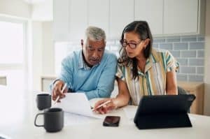 A senior couple reviews financial documents together at a kitchen counter with a tablet signifying how couples handle money.