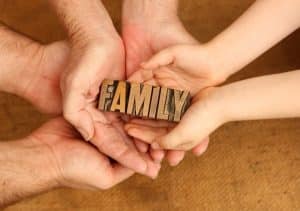 Multiple generations of hands holding a wooden block that says family, symbolizing estate planning and family legacy meetings.
